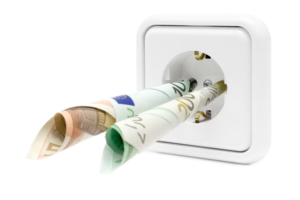 Banconote arrotolate inserite in una presa elettrica a muro, sfondo bianco, immagine concettuale sul denaro