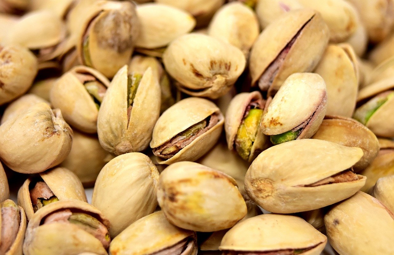 Primo piano di un mucchio di pistacchi tostati, tonalità beige e marroni chiari, alcuni gusci aperti